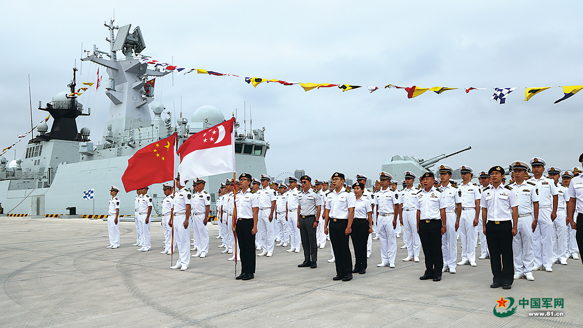 Naval personnel with Chinese and Singaporean flags, standing at a pier beside a naval ship.